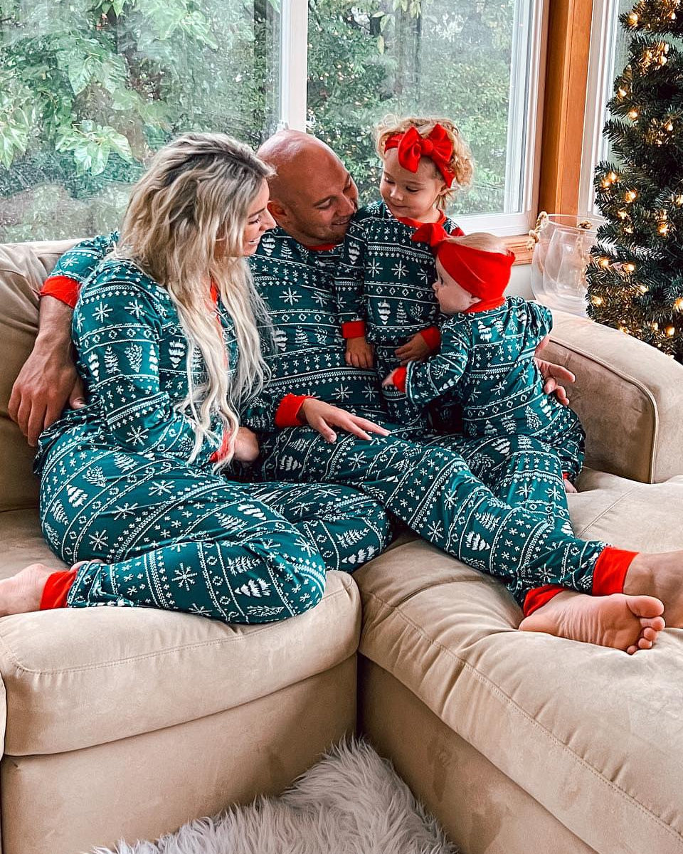 Family sitting on a couch in matching pajamas with a Christmas tree in the background.