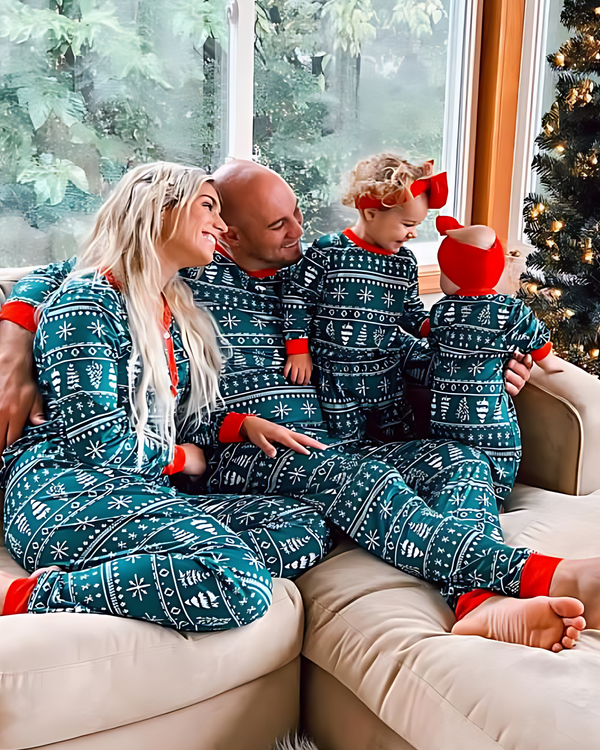 A family of four wearing matching teal and white Christmas-themed patterned pajamas, sitting together on a beige couch in front of a window with a decorated Christmas tree visible in the background.